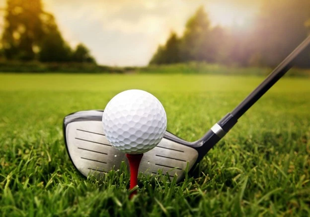 A golf ball rests atop a tee as a pitching wedge draws near. 