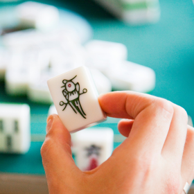 A mahjong player holding a single tile in their hand