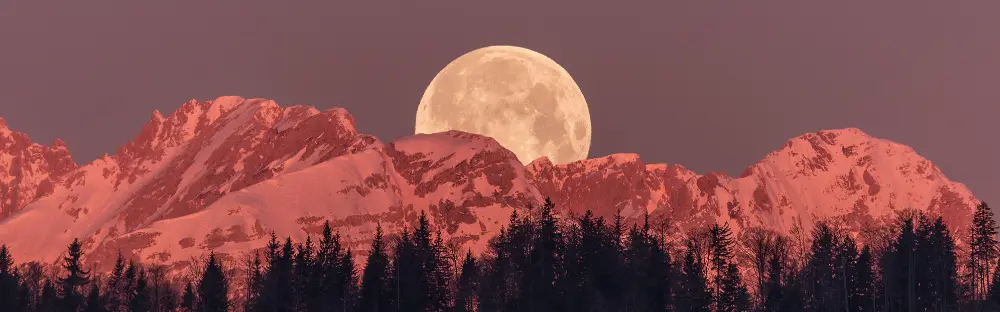 A photograph of a moon over a mountain range