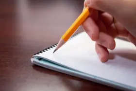A closeup of someone writing in a notebook with a pencil